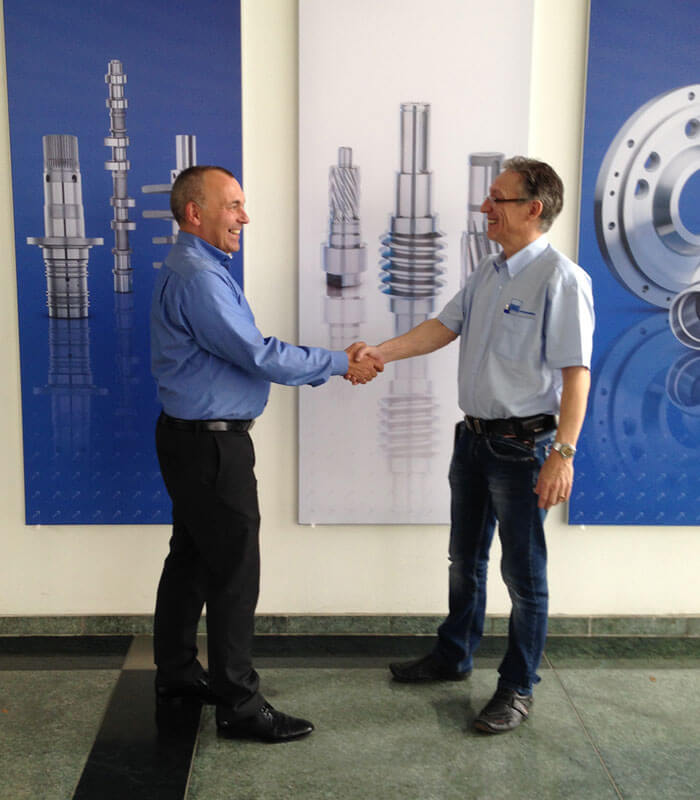 Inhouse-Train-the-Trainer-Seminar: Zwei Teilnehmende begrüßen sich per Handschlag vor technischen Schautafeln