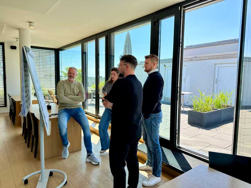 Train-the-Trainer-Seminar: Teilnehmende stehen gemeinsam am Flipchart in einem modernen Seminarraum und diskutieren Inhalte in Kleingruppenarbeit.