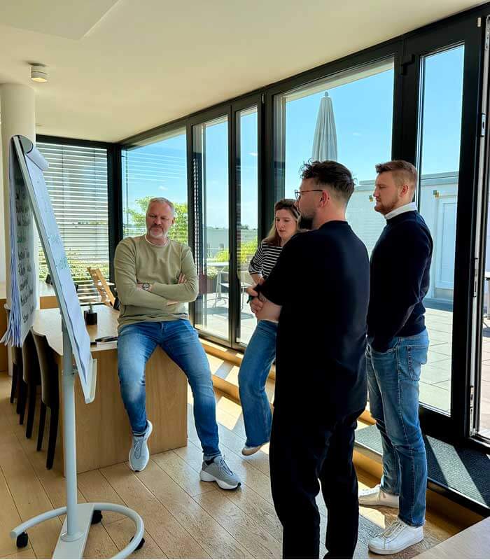 Train-the-Trainer-Seminar: Teilnehmende stehen gemeinsam am Flipchart in einem modernen Seminarraum und diskutieren Inhalte in Kleingruppenarbeit.